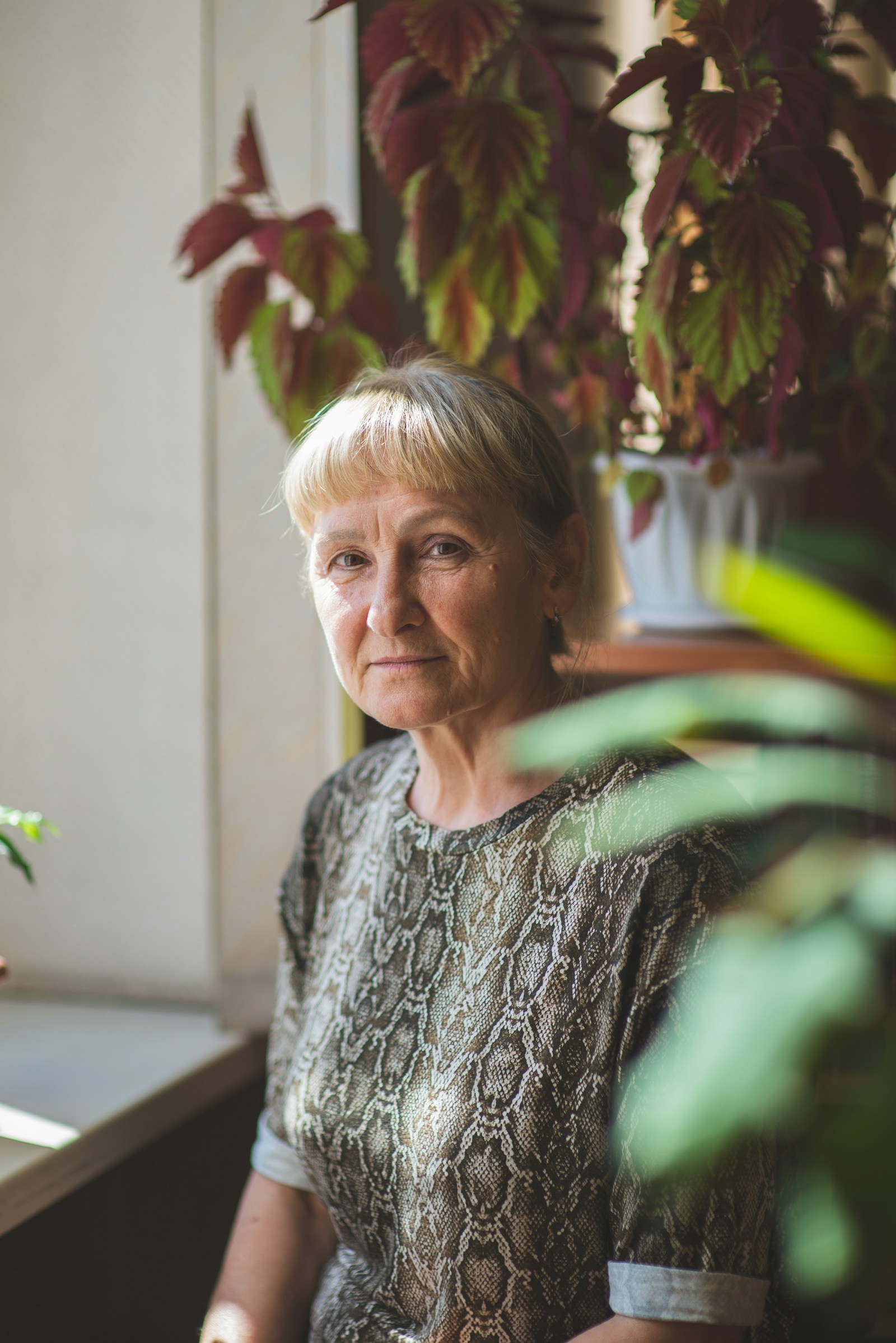 A woman in her sixties sitting calmly among houseplants in warm natural light