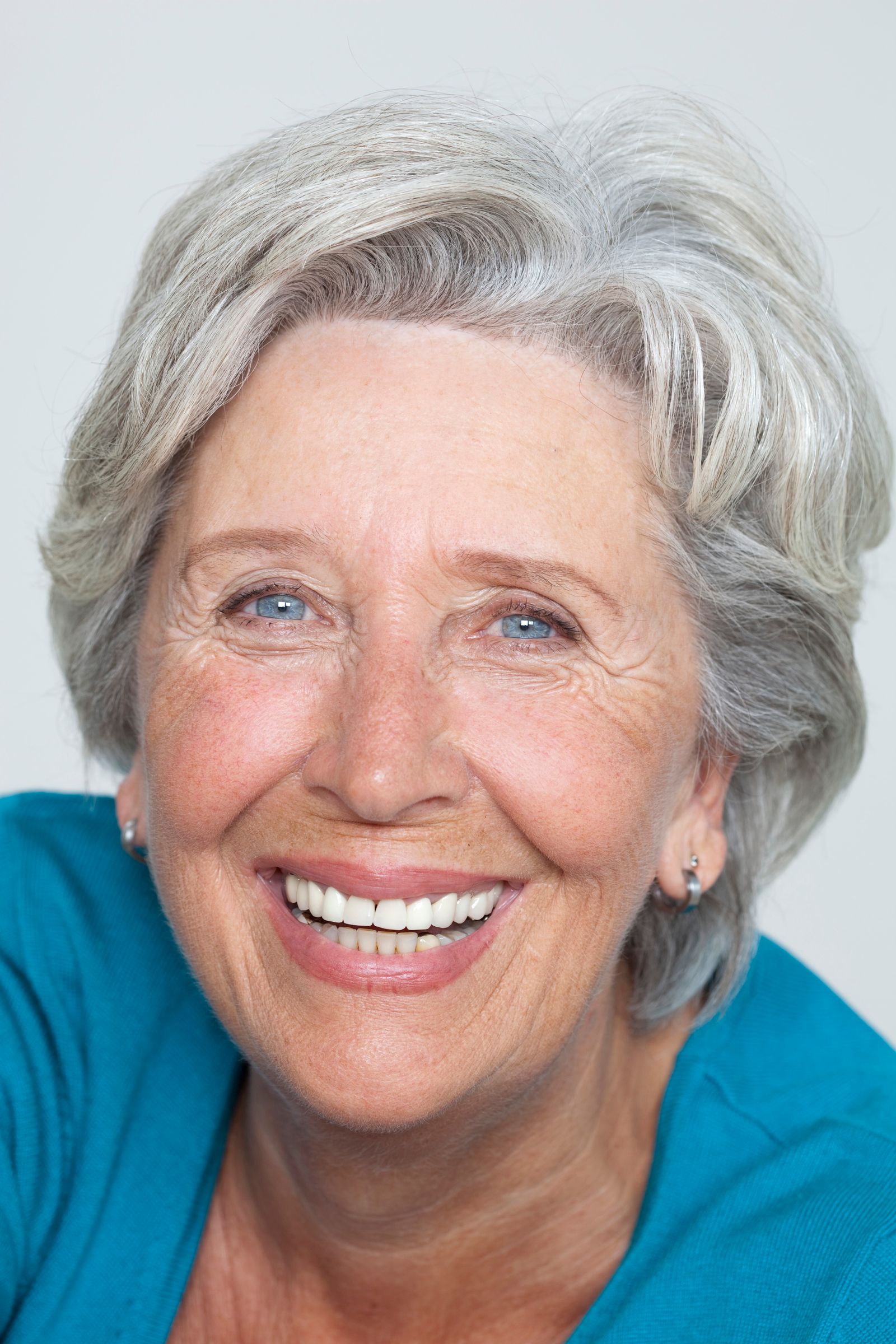 A smiling woman in her early sixties with silver hair in a soft portrait